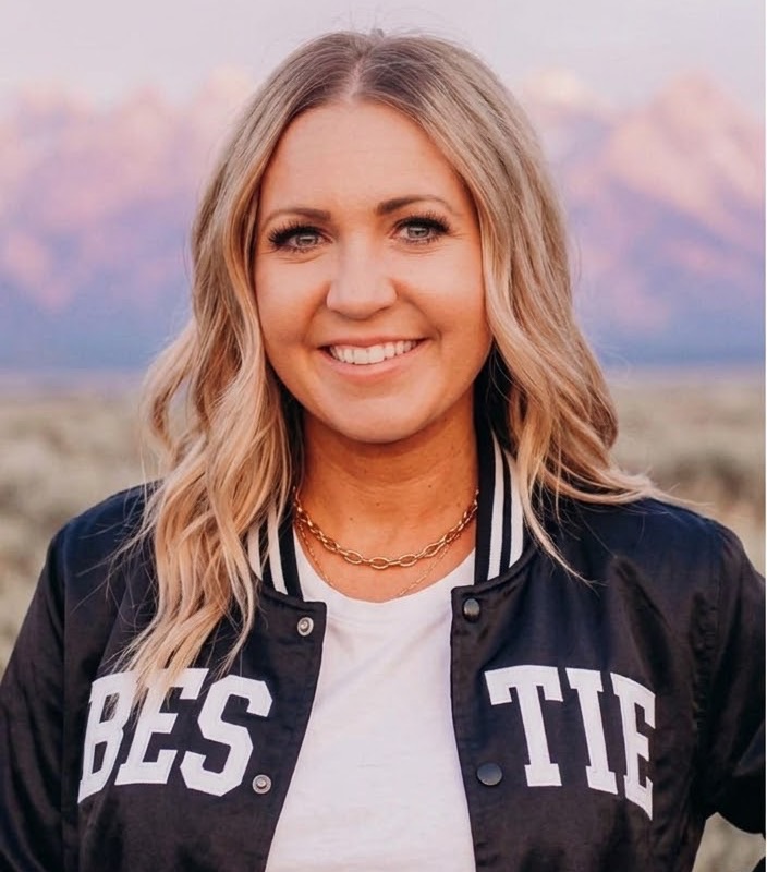 Dani, founder of the Bestie Squad, in a navy BESTIE varsity jacket with mountains behind her.
