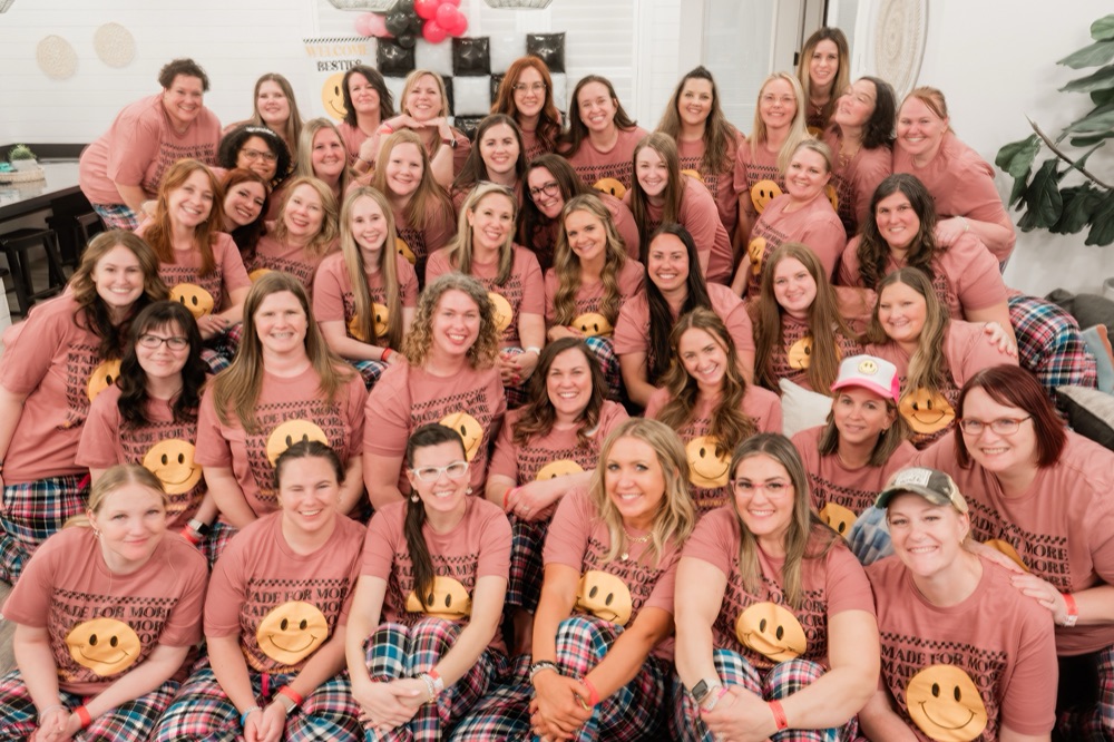 A large group of Bestie Squad members at a retreat, all wearing matching pink Made For More t-shirts and smiling together.