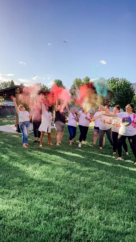 Bestie Squad women tossing colored powder into the air on a grassy field.